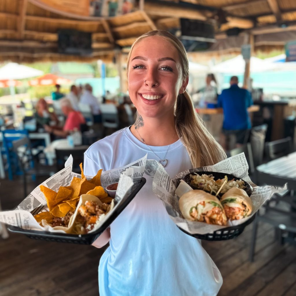 Server smiling while holding food baskets at Evie’s on the Bay.