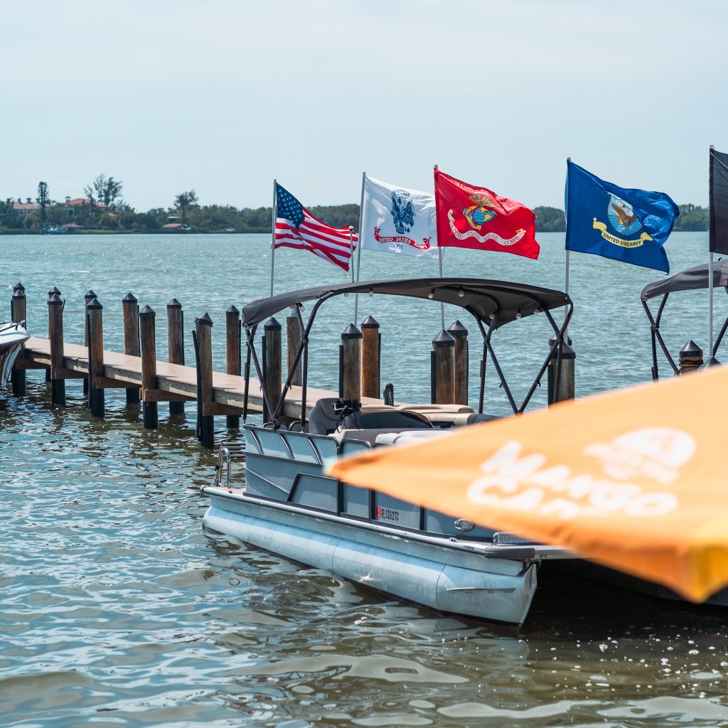 Pontoon boat docked near Evie’s On the Bay with service flags flying over the water.