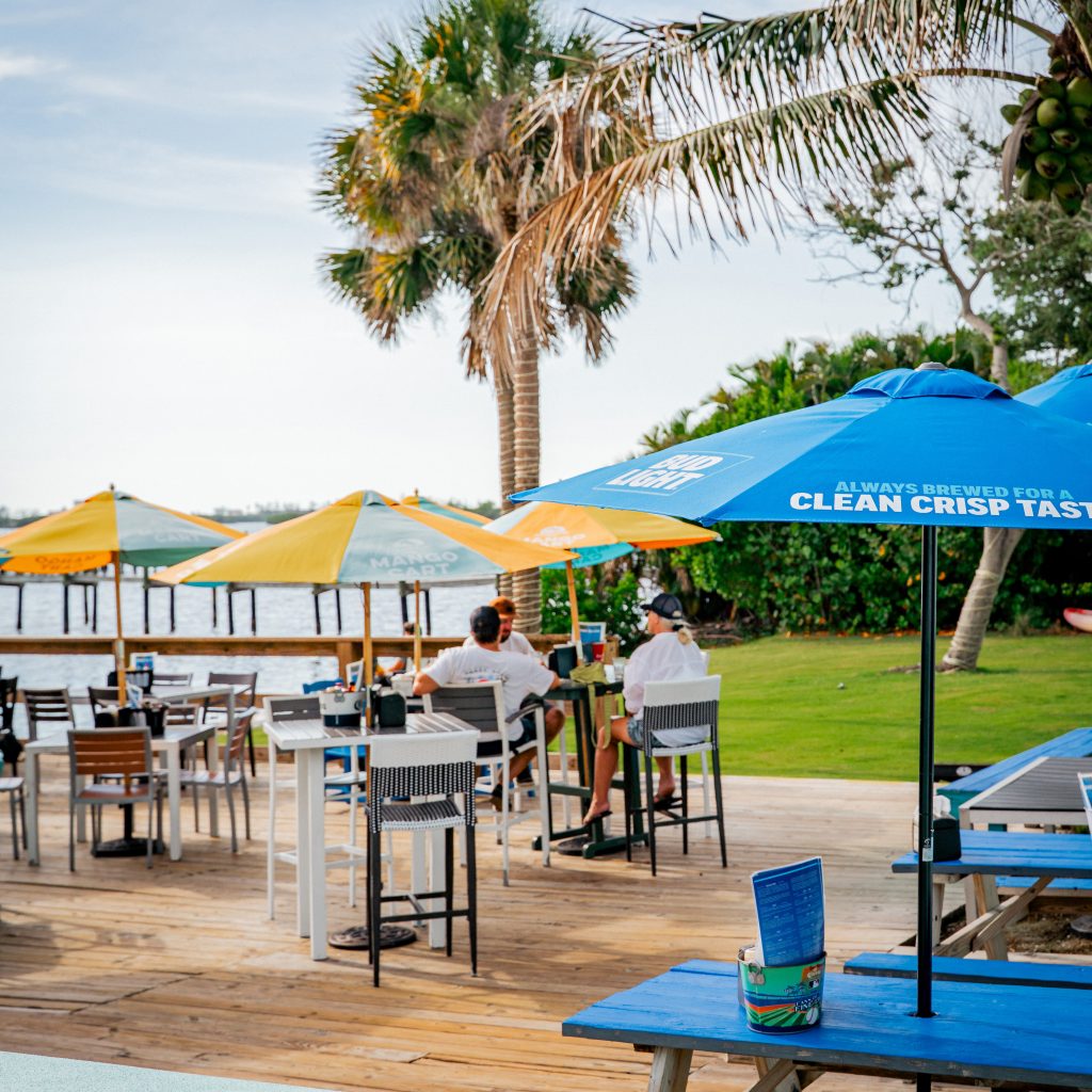 Guests seated at outdoor tables under blue and yellow umbrellas at Evie’s On the Bay.