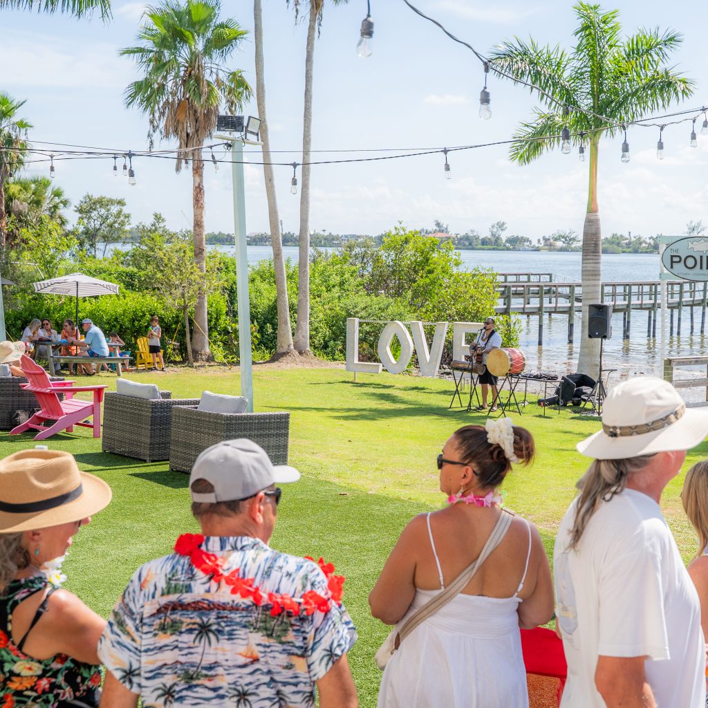 Guests watching live music on the waterfront lawn at Evie’s On the Bay with the LOVE sign nearby.